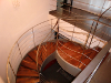 Escalera helicoidal que presenta un contragiro, con zancas de hierro, barandilla de acero inoxidable y peldaños de madera